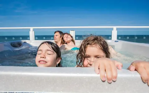 Famiglia felice in vasca idromassaggio, godendosi il Ferragosto con bambini. Il sole splende, il mare sullo sfondo.