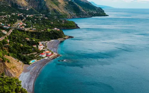 Villaggio costiero con case bianche e rosse affacciato su una spiaggia di ciottoli scuri e mare blu intenso. Le **basilicata spiagge** offrono panorami mozzafiato.