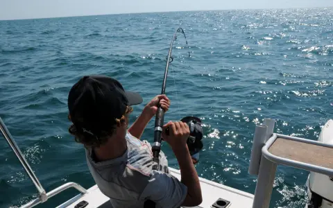 Ragazzo con cappellino nero pesca in mare, mostrando alcuni metodi di pesca con la canna.