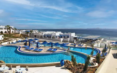 Vista panoramica del Futura Club Albatros Palace Sharm: piscine azzurre, lettini, ombrelloni blu e il mare scintillante all'orizzonte.
