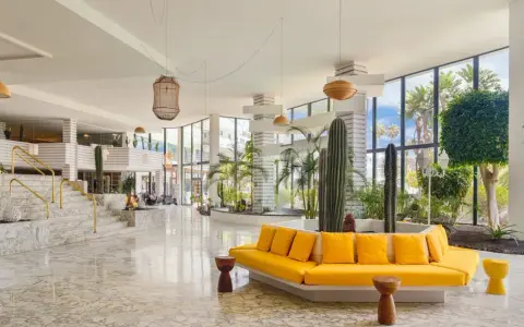 Lobby moderna con cactus e piante tropicali, divano giallo vivace e marmo lucido. Un'oasi di stile al H10 Lanzarote Princess.