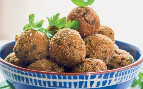 Polpette di melanzane dorate e croccanti, guarnite con prezzemolo fresco, in una ciotola blu decorata.