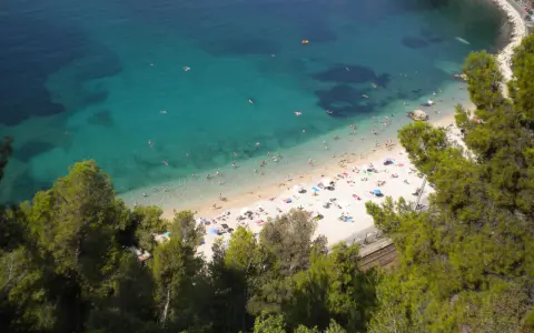 Spiaggia affollata sulla costa azzurra con bambini che giocano in acqua e prendono il sole.