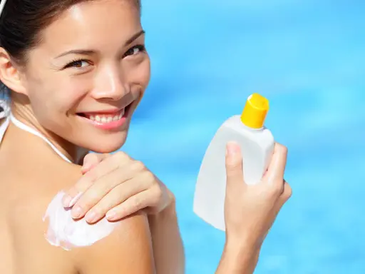 Donna sorridente applica crema solare sulla spalla, con una bottiglia in mano. Scopri che protezione solare usare per la tua pelle.