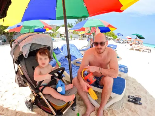 Un papà e il suo bambino si godono una giornata di sole alle Maldive con bambini, tra giochi sulla sabbia e relax sotto gli ombrelloni colorati.