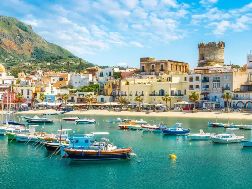 Un incantevole scorcio di Ischia con bambini che sognano gite in barca. Case colorate, mare azzurro e un castello medievale.