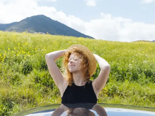Ragazza con cappello di paglia al sole, godendosi la natura. Un modo per pensare a come abbronzarsi velocemente il viso in estate.