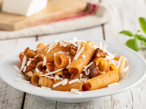 Un piatto invitante di pasta alla norma con melanzane fritte, pomodoro e ricotta salata grattugiata, pronto per essere gustato.