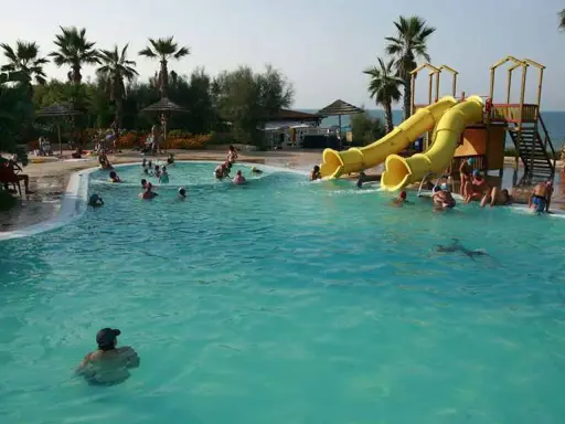 Piscina con scivoli gialli e persone che nuotano, ideale per campeggi puglia sul mare per bambini.