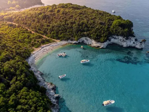Baia con acque cristalline e vegetazione lussureggiante, ideale per famiglie. Diverse barche ormeggiate, perfette per esplorare le isole greche.