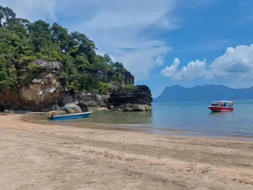 Spiaggia in Malesia con bambini su una barca rossa. Rocce verdi e mare azzurro.