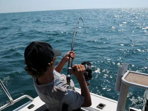 Ragazzo con cappellino nero pesca in mare, mostrando alcuni metodi di pesca con la canna.