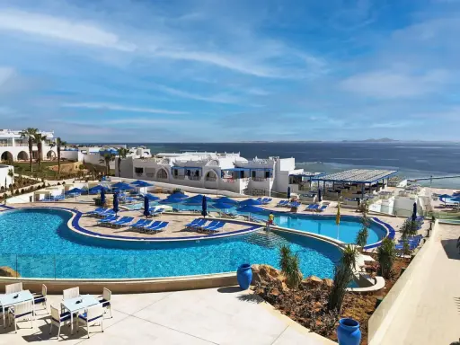 Vista panoramica del Futura Club Albatros Palace Sharm: piscine azzurre, lettini, ombrelloni blu e il mare scintillante all'orizzonte.