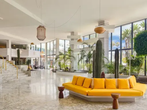 Lobby moderna con cactus e piante tropicali, divano giallo vivace e marmo lucido. Un'oasi di stile al H10 Lanzarote Princess.