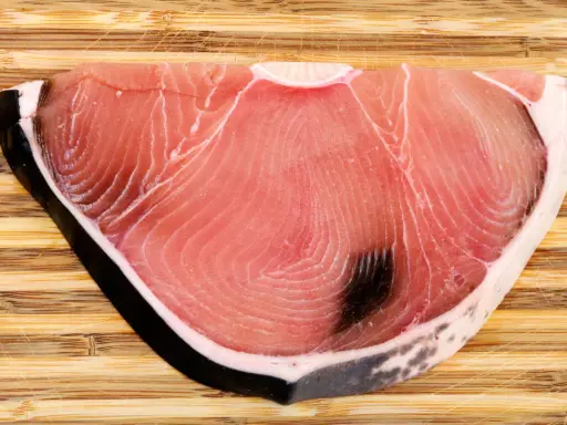 Fetta di tonnina, un pregiato pesce azzurro, su tagliere di legno. La sua carne rosa vivo mostra le tipiche striature.