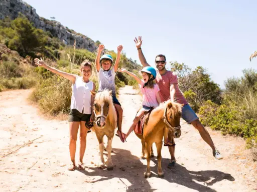 Famiglia felice a Minorca con bambini a cavallo, un'avventura indimenticabile tra sentieri soleggiati e natura rigogliosa.
