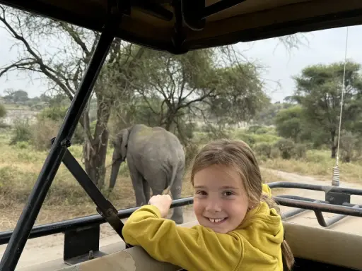 Un'avventura indimenticabile a Zanzibar con bambini: un elefante appare sullo sfondo mentre una bambina sorride dal fuoristrada.
