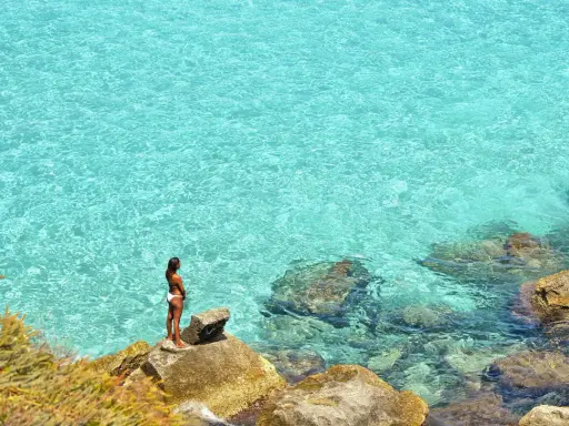 Donna su scogli ammira acque cristalline, un gioiello delle aree marine protette in Italia.