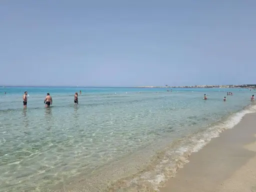 Persone in piedi nell'acqua cristallina, con la costa di Gallipoli sullo sfondo. Un perfetto giorno di mare.
