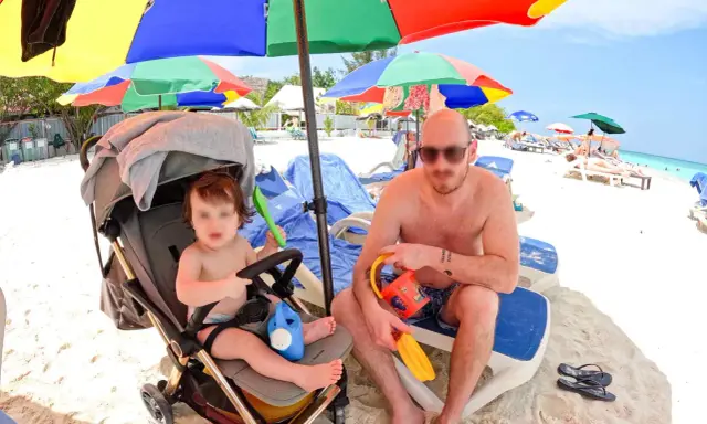 Un papà e il suo bambino si godono una giornata di sole alle Maldive con bambini, tra giochi sulla sabbia e relax sotto gli ombrelloni colorati.
