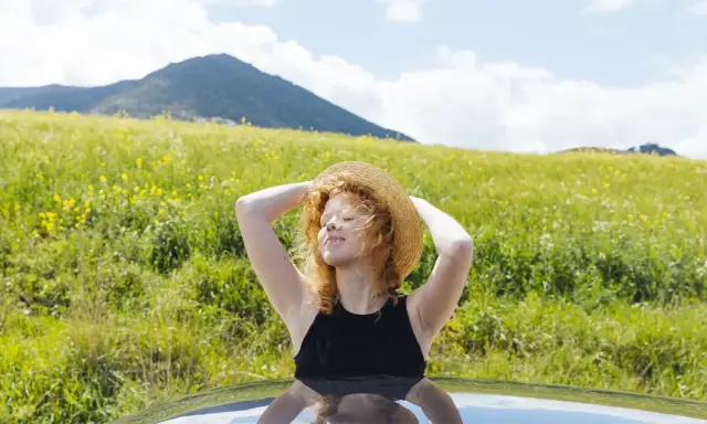 Ragazza con cappello di paglia al sole, godendosi la natura. Un modo per pensare a come abbronzarsi velocemente il viso in estate.
