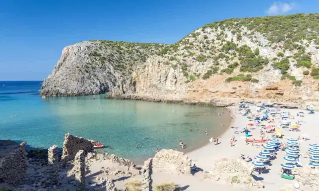Spiaggia affollata con ombrelloni colorati, acque cristalline e scogliere verdi. Perfetta per vacanze al mare economiche e rilassanti.