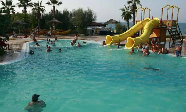 Piscina con scivoli gialli e persone che nuotano, ideale per campeggi puglia sul mare per bambini.