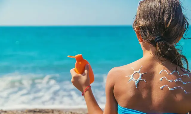 Bambina sulla spiaggia applica crema solare, disegnando un sole e onde sulla schiena. Un modo per non abbronzarsi e proteggersi.
