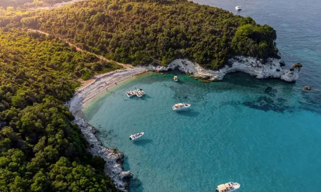 Baia con acque cristalline e vegetazione lussureggiante, ideale per famiglie. Diverse barche ormeggiate, perfette per esplorare le isole greche.