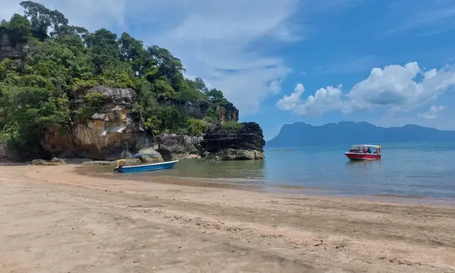 Spiaggia in Malesia con bambini su una barca rossa. Rocce verdi e mare azzurro.