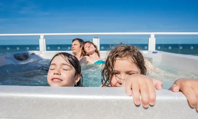 Famiglia felice in vasca idromassaggio, godendosi il Ferragosto con bambini. Il sole splende, il mare sullo sfondo.