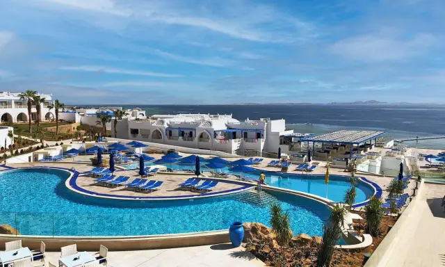 Vista panoramica del Futura Club Albatros Palace Sharm: piscine azzurre, lettini, ombrelloni blu e il mare scintillante all'orizzonte.