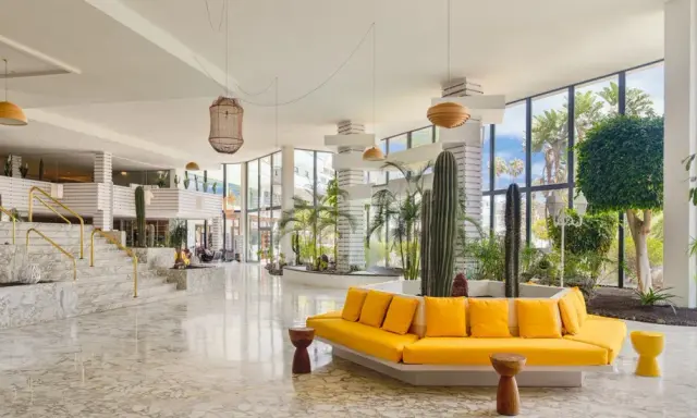 Lobby moderna con cactus e piante tropicali, divano giallo vivace e marmo lucido. Un'oasi di stile al H10 Lanzarote Princess.