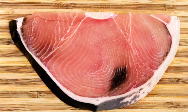 Fetta di tonnina, un pregiato pesce azzurro, su tagliere di legno. La sua carne rosa vivo mostra le tipiche striature.