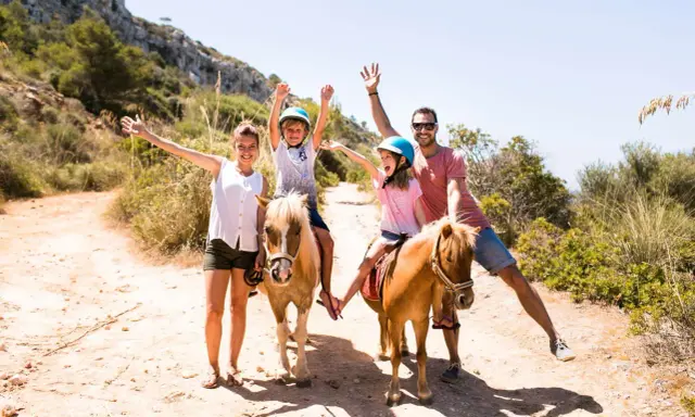 Famiglia felice a Minorca con bambini a cavallo, un'avventura indimenticabile tra sentieri soleggiati e natura rigogliosa.