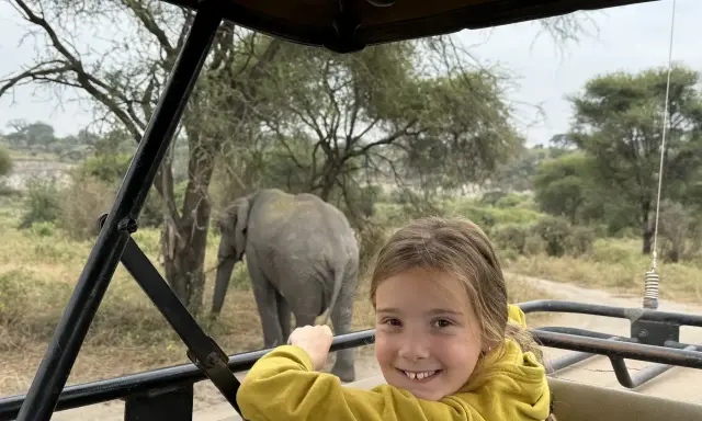 Un'avventura indimenticabile a Zanzibar con bambini: un elefante appare sullo sfondo mentre una bambina sorride dal fuoristrada.