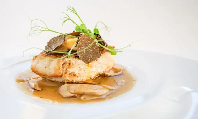 Un succulento mero pescado, guarnito con tartufo e germogli freschi, adagiato su un letto di funghi e salsa cremosa.
