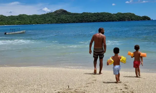 Un padre cammina sulla spiaggia con i suoi due figli, pronti per un'avventura in Costa Rica con bambini.