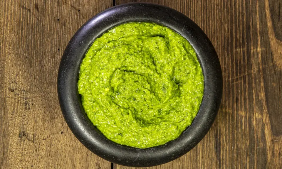 Pestello in pietra con un vibrante pesto alla genovese, pronto per condire la pasta.