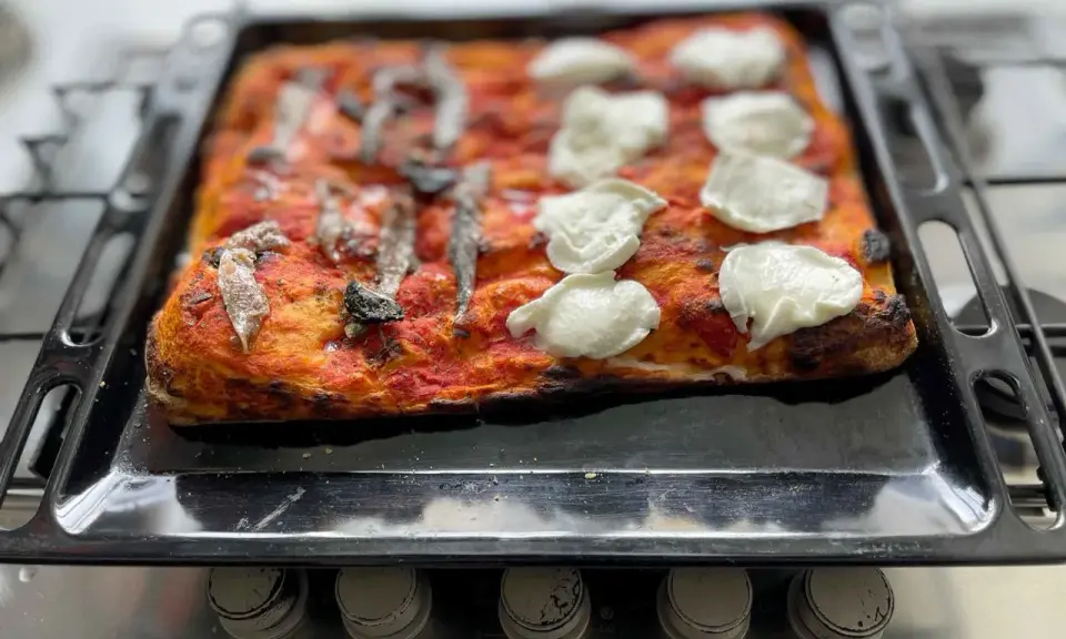 Pizza fatta in casa con pomodoro, acciughe e mozzarella appena sfornata su una teglia.