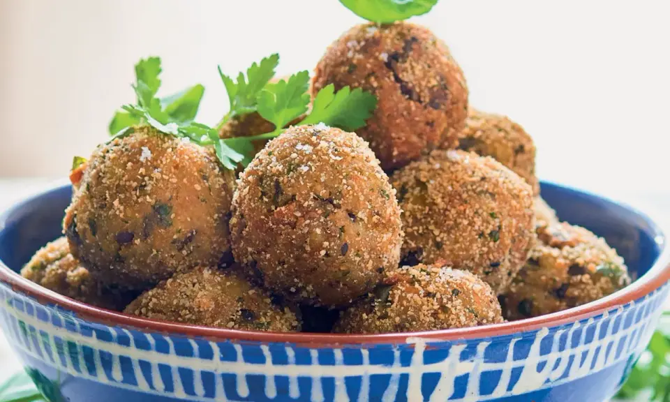 Polpette di melanzane dorate e croccanti, guarnite con prezzemolo fresco, in una ciotola blu decorata.