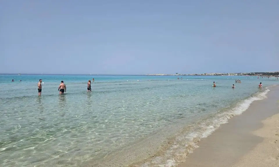 Persone in piedi nell'acqua cristallina, con la costa di Gallipoli sullo sfondo. Un perfetto giorno di mare.