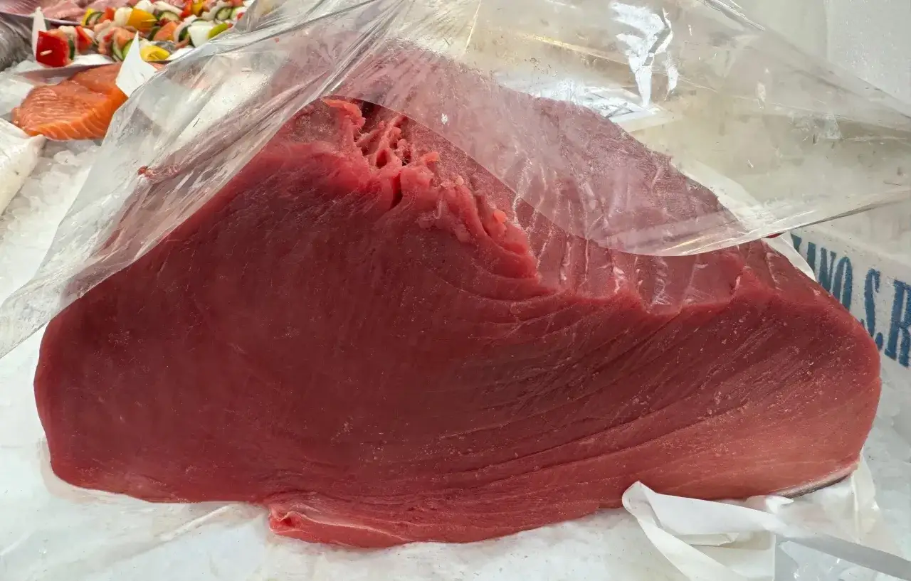 Un grande trancio di tonno rosso fresco, avvolto in plastica, pronto per essere cucinato. Le sue propriet&agrave; nutrizionali lo rendono un alimento prezioso.