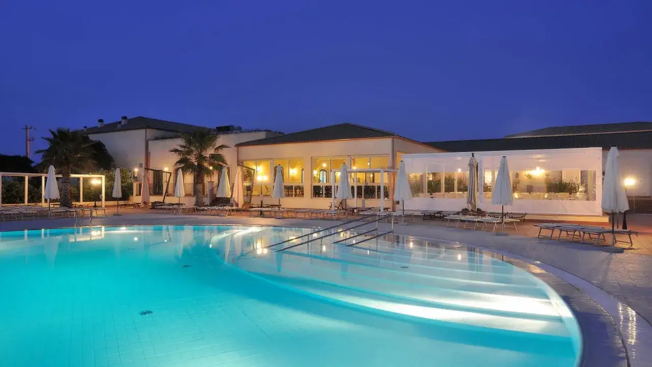 Piscina illuminata di notte al Sikania Eco Resort, con palme e lettini.