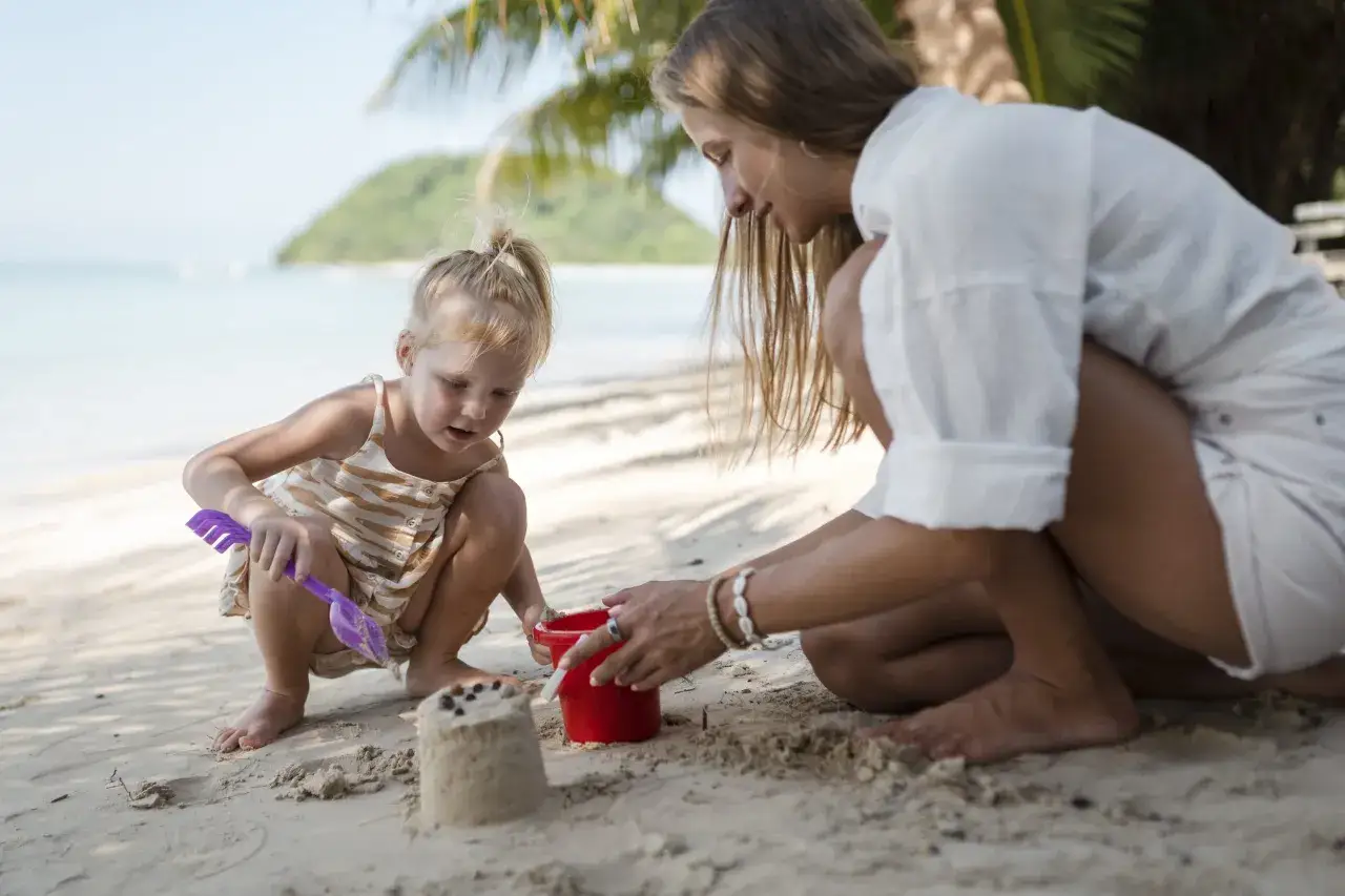 Un perfetto ferragosto con bambini: madre e figlia giocano con la sabbia sulla spiaggia, costruendo un castello.