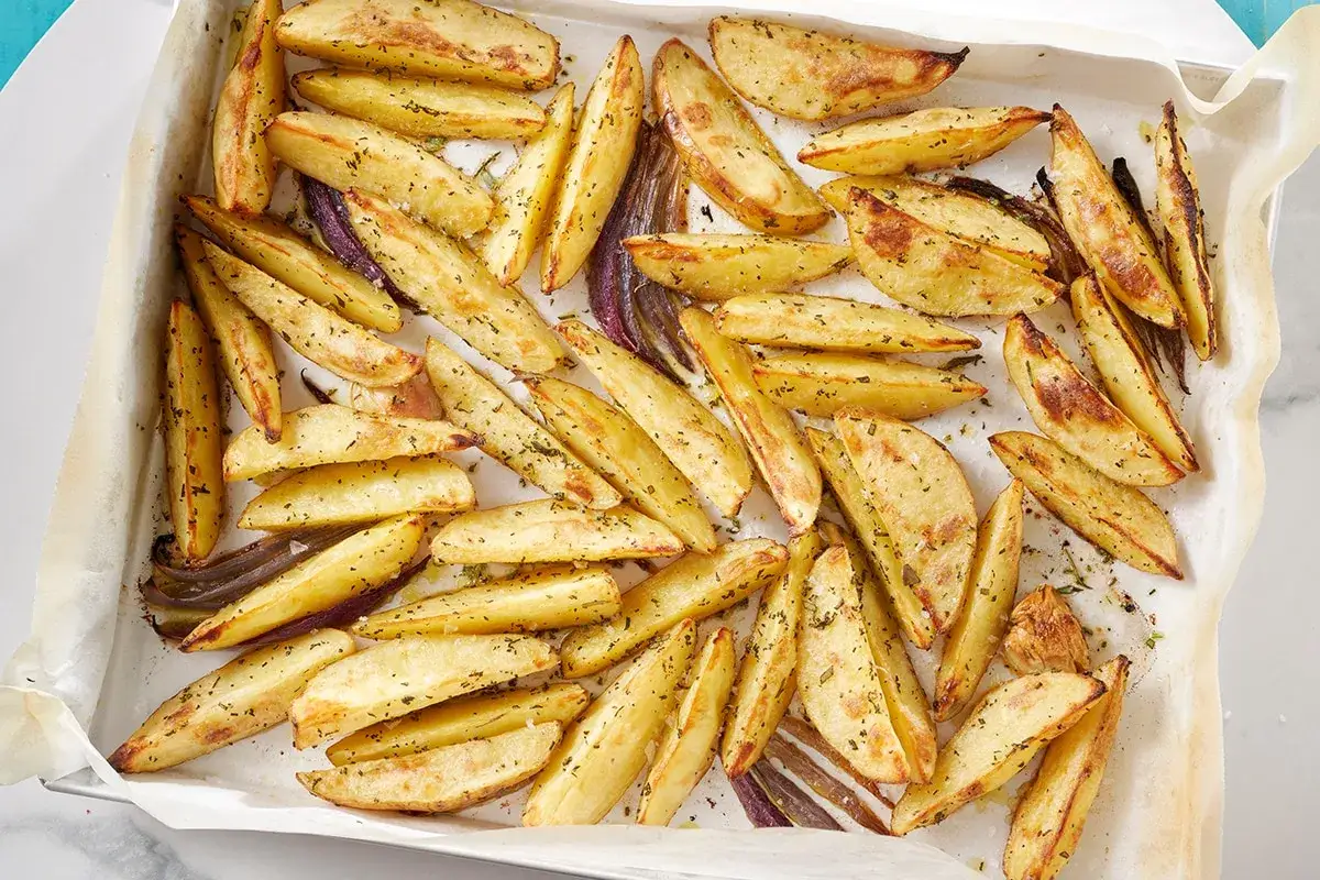 Patate al forno dorate e croccanti, condite con erbe aromatiche, su carta da forno. Un contorno perfetto per ogni pasto.