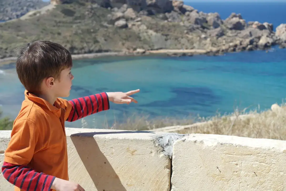 Bambino indica il mare turchese a Malta, un ricordo di vacanze con bambini.