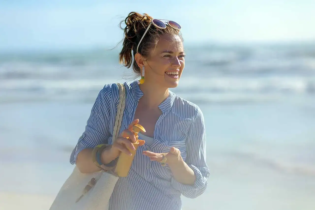 Donna sorridente in spiaggia applica crema solare, un modo per non abbronzarsi e proteggere la pelle.