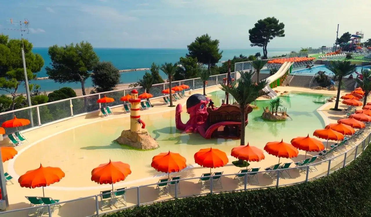 Un parco acquatico con scivoli e un polpo gigante, vicino a una riva verde fermo con il mare all'orizzonte.