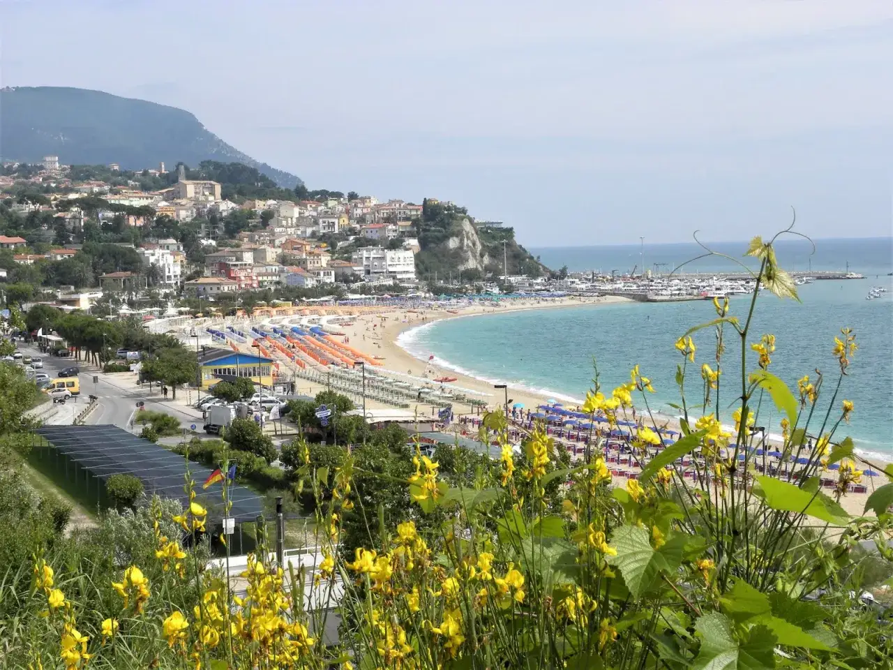 Vista panoramica delle spiagge di Numana con ombrelloni colorati, mare azzurro e un borgo arroccato sulla collina.